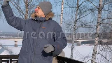 穿着蓝色羽绒服的人，带着毛皮罩，在冬季公园里用手机进行视频聊天和微笑。